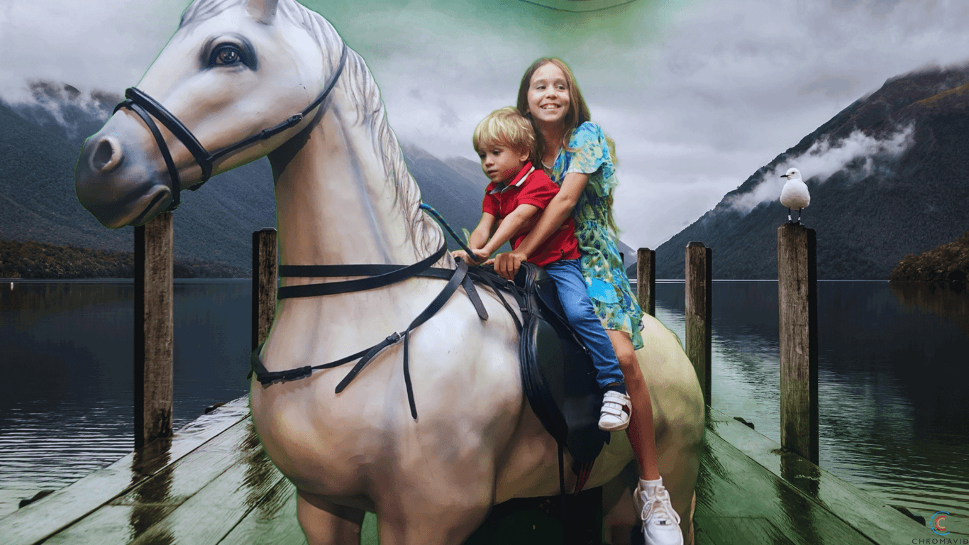 Children riding a horse on a lakeside dock surrounded by misty mountains