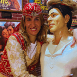 Woman in traditional costume posing with a Bollywood actor statue inside a film-themed display area