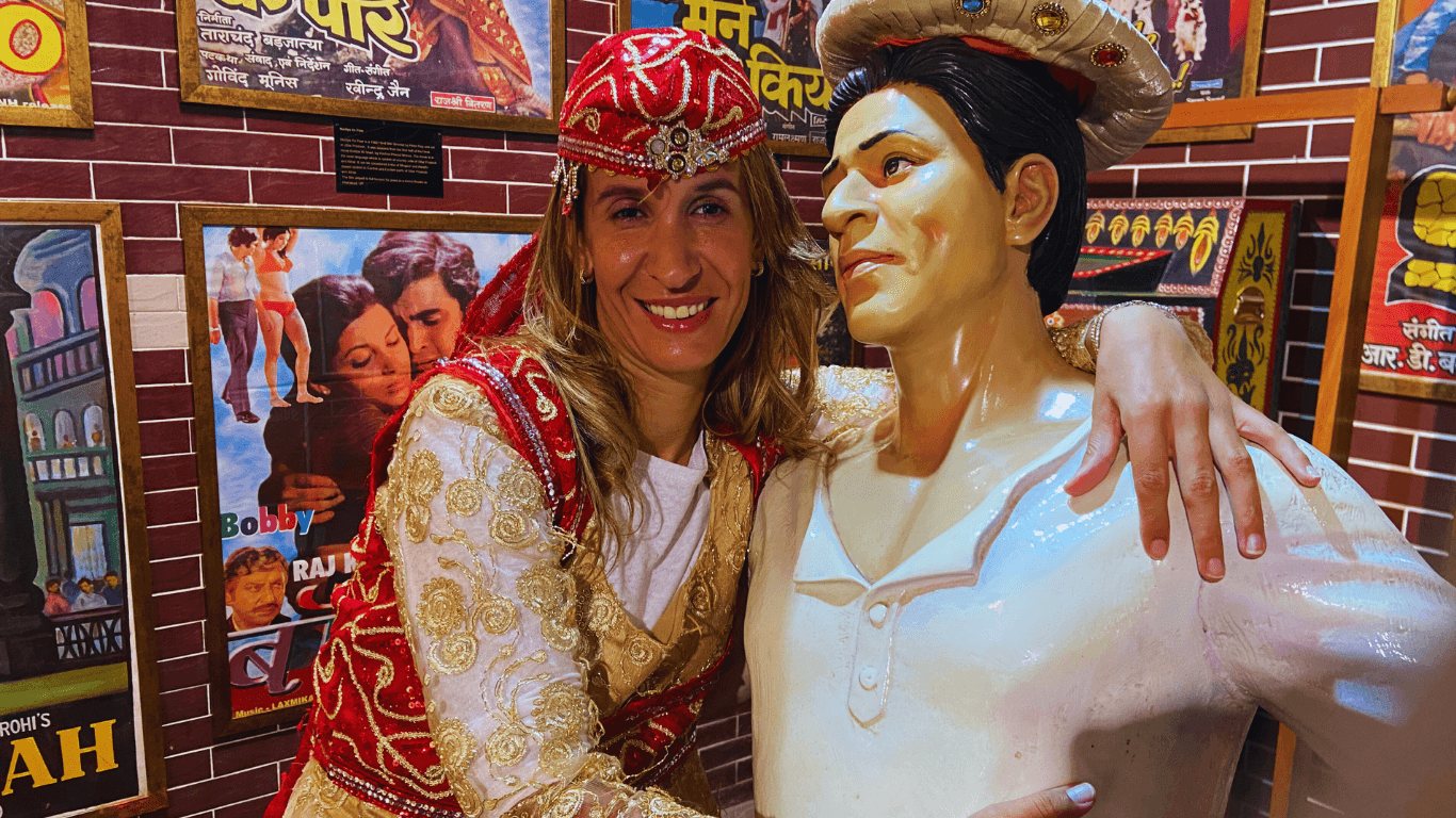 Woman in traditional costume posing with a Bollywood actor statue inside a film-themed display area