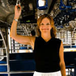 Woman smiling while standing inside a train carriage holding an overhead handle