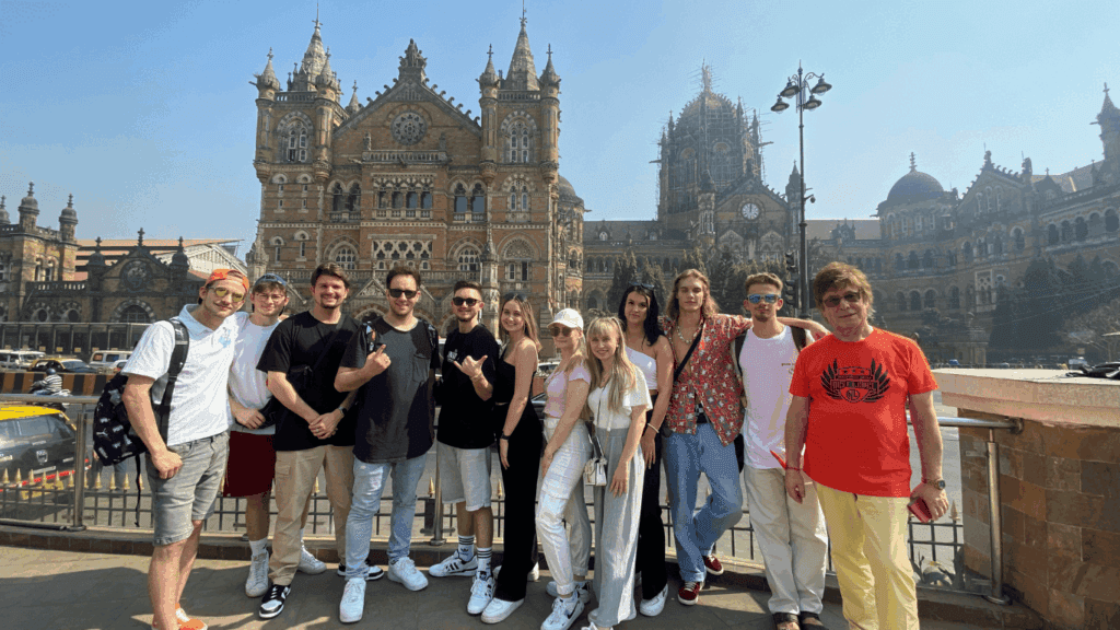 Group of international travelers posing together in front of Chhatrapati Shivaji Maharaj Terminus during a memorable Mumbai city tour.