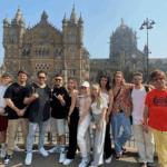 Group of international travelers posing together in front of Chhatrapati Shivaji Maharaj Terminus during a memorable Mumbai city tour.