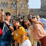 Group of international travelers taking a selfie together in front of Chhatrapati Shivaji Maharaj Terminus during a Mumbai city tour.