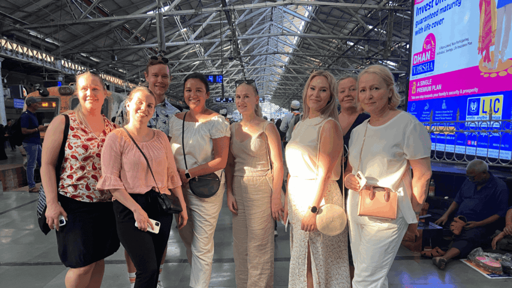 Group of international travelers posing inside a busy Mumbai railway station during a guided city tour.